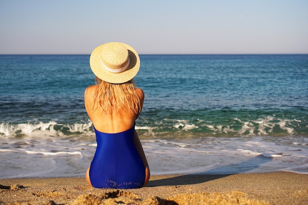 Giovane donna che prende il sole in spiaggia tropicale donna in costume da bagno blu e cappello