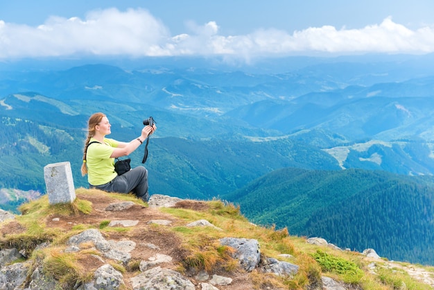Giovane donna che prende selfie di viaggio sulla macchina fotografica sulla scogliera delle montagne