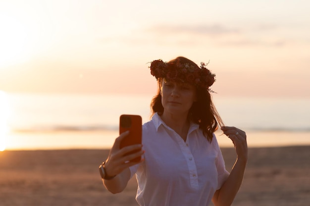 Giovane donna che prende selfie tramite smartphone mentre si trova in spiaggia durante il tramonto