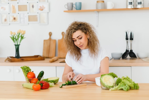 Giovane donna che prepara insalata di verdure nella sua cucina.