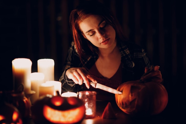 Giovane donna che prepara la zucca di Halloween Jackolantern con le candele nel buio Mani femminili che tagliano zucche con un coltello