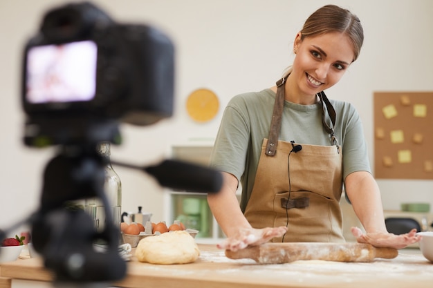 Giovane donna che prepara una torta al tavolo e sorridendo alla telecamera ha girato il video per il suo blog