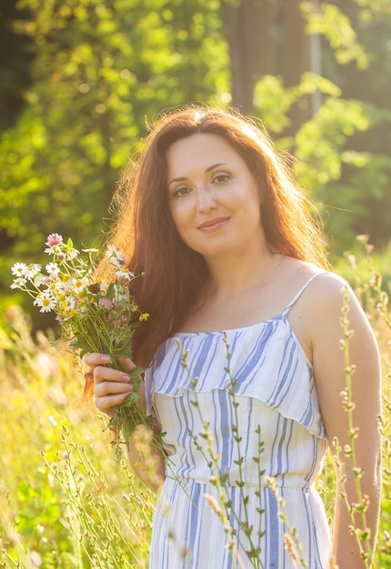 Giovane donna che raccoglie fiori nel prato nella sera d'estate