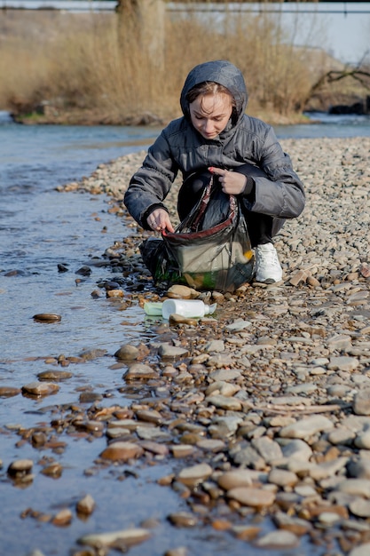 Giovane donna che raccoglie i rifiuti di plastica dalla spiaggia e li mette in sacchetti di plastica neri per riciclarli. Concetto di pulizia e riciclaggio.