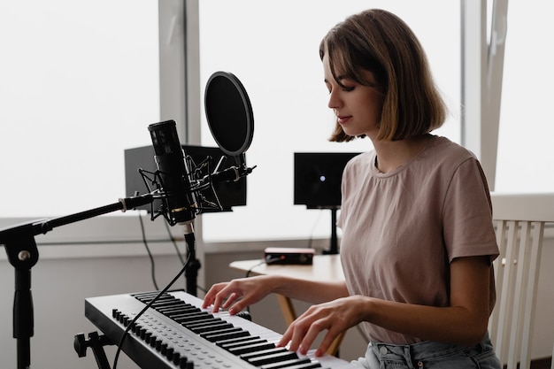 Giovane donna che registra una canzone suonare il pianoforte e cantare a casa