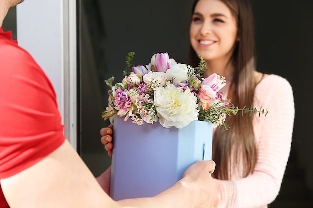 Giovane donna che riceve bellissimi fiori dal fattorino a casa