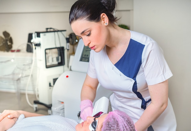 Giovane donna che riceve un trattamento laser in cosmetologia clinica. Occhi coperti con occhiali protettivi