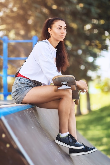 Giovane donna che riposa con uno skateboard in mano nel parco