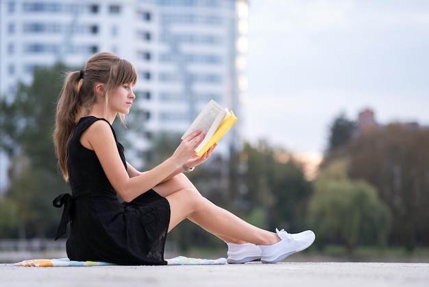 Giovane donna che riposa nel parco estivo leggendo un libro Istruzione e concetto sudy