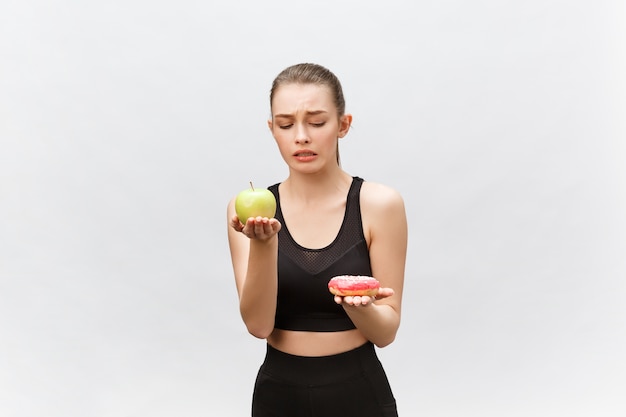 Giovane donna che sceglie fra il dessert e la mela Concetto dell'alimento di dieta.