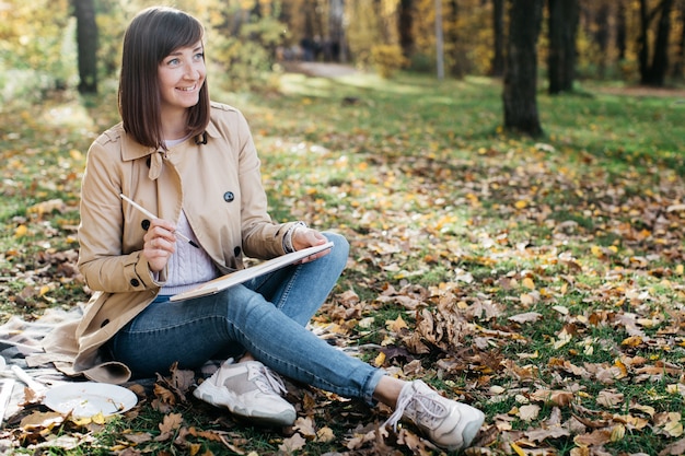 Giovane donna che schizza vicino a un lago nella foresta di autunno Schizzi