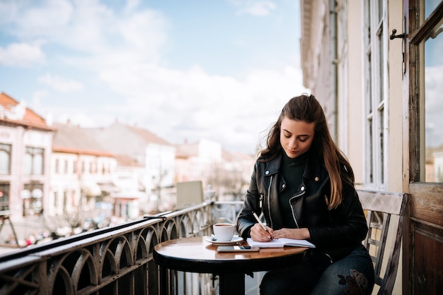 Giovane donna che scrive in un diario mentre era seduto sulla terrazza della città.