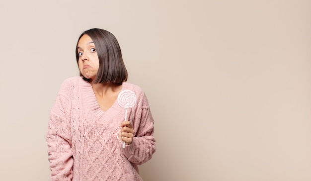 Giovane donna che scrolla le spalle, sentendosi confusa e incerta, dubbiosa con le braccia incrociate e lo sguardo perplesso