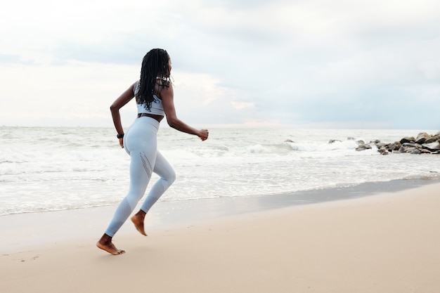 Giovane donna che si diverte a correre sulla spiaggia al mattino in una giornata estiva