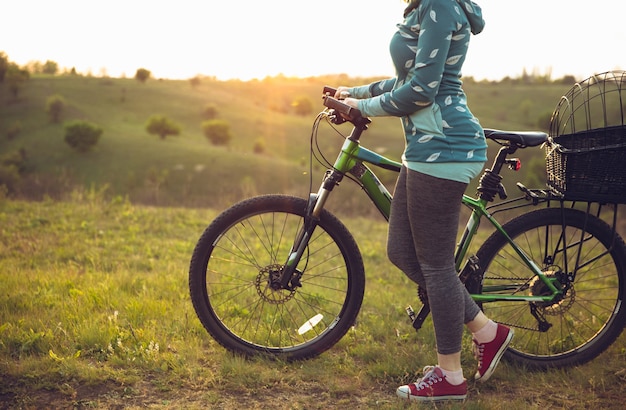 Giovane donna che si diverte vicino al parco di campagna, andare in bicicletta, viaggiare al giorno di primavera