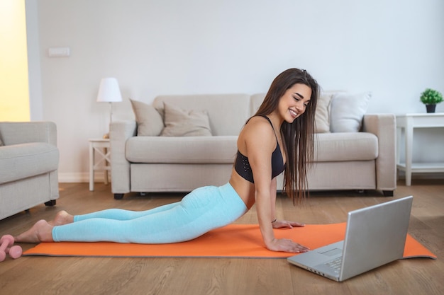 Giovane donna che si esercita a casa in un soggiorno Lezione video Giovane donna che ripete gli esercizi mentre guarda la sessione di allenamento online Bella giovane donna che fa esercizio di fitness a casa