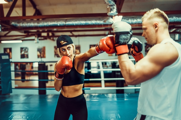 Giovane donna che si esercita con l'istruttore alla lezione di boxe e dell'autodifesa