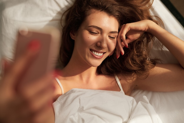 Giovane donna che si fa selfie a letto