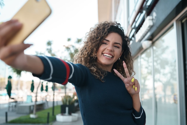 Giovane donna che si fa selfie con il suo telefono mofilo mentre sta in piedi all'aperto. Concetto urbano.