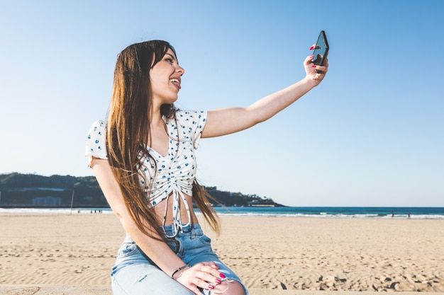 Giovane donna che si fa un selfie con un telefono cellulare sul lato della spiaggia