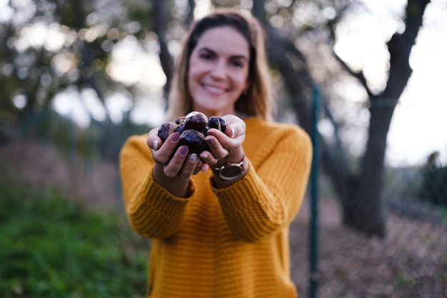 Giovane donna che si gode l'autunno che raccoglie le castagne in un maglione giallo al tramonto