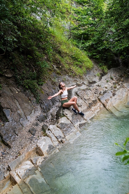 Giovane donna che si gode la natura, seduta in riva al fiume di montagna