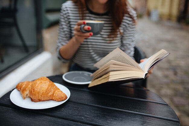 Giovane donna che si gode un caffè gustoso e legge un libro sulla terrazza del caffè