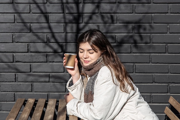 Giovane donna che si gode un drink contro il muro di mattoni dell'esterno della caffetteria