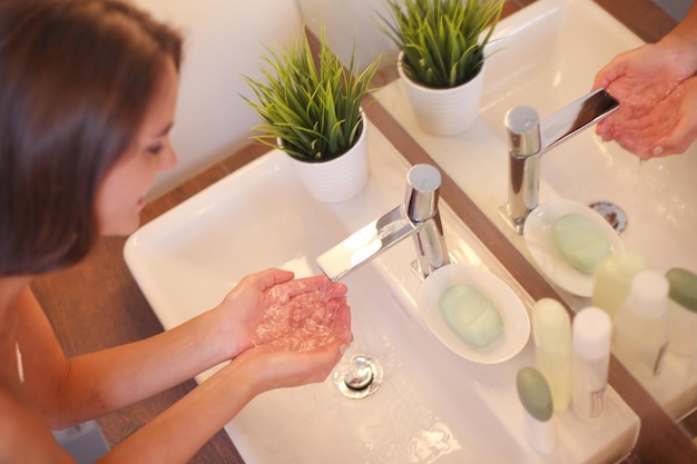 Giovane donna che si lava il viso con acqua pulita in bagno