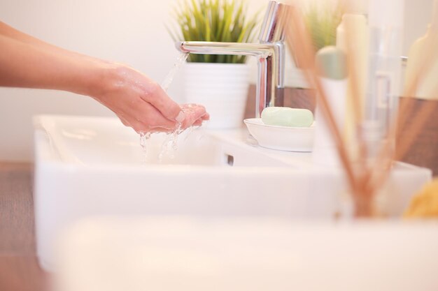 Giovane donna che si lava il viso con acqua pulita in bagno