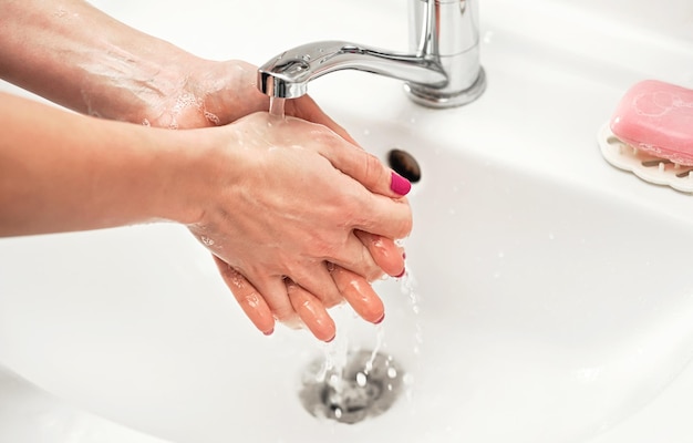 Giovane donna che si lava le mani sotto il rubinetto dell'acqua con sapone. Dettaglio sul liquido sulla pelle. concetto di igiene personale.