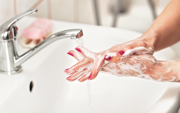 Giovane donna che si lava le mani sotto il rubinetto dell'acqua con sapone. Dettaglio sulla pelle insaponata. Concetto di igiene personale - prevenzione delle epidemie di coronavirus covid 19