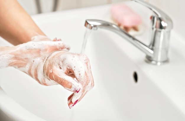 Giovane donna che si lava le mani sotto il rubinetto dell'acqua con sapone. Dettaglio sulla pelle insaponata. Concetto di igiene personale - prevenzione delle epidemie di coronavirus covid 19