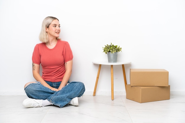 Giovane donna che si muove nella nuova casa tra le caselle isolate su sfondo bianco guardando il lato