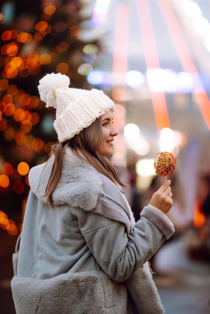 Giovane donna che si rilassa bevendo caffè nella fiera natalizia festiva. Vacanze invernali. Luci intorno.