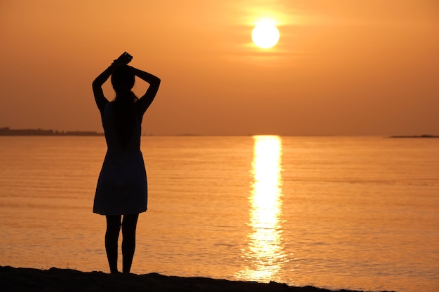 Giovane donna che si rilassa da sola sulla riva di sabbia dell'oceano in riva al mare godendosi una calda serata tropicale.