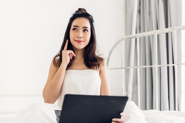 Giovane donna che si rilassa facendo uso del computer portatile in camera da letto