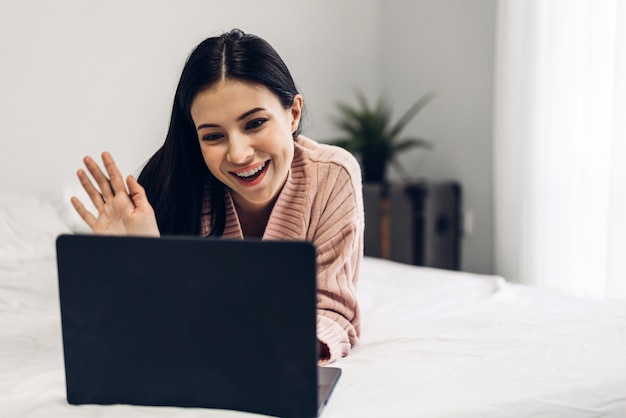 Giovane donna che si rilassa facendo uso del computer portatile nella camera da letto donna che controlla i apps e lavoro sociali Concetto di tecnologia e di comunicazione