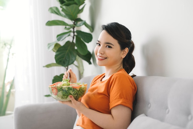 Giovane donna che si rilassa sul divano a casa e mangia un'insalata di giardino fresca, uno stile di vita sano e un concetto di nutrizione