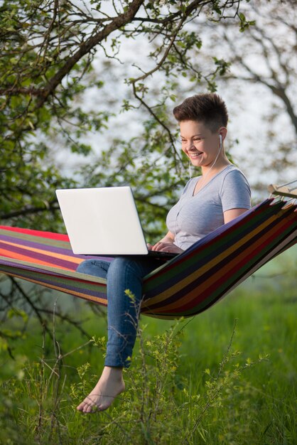 Giovane donna che si siede in un'amaca che lavora al suo computer portatile