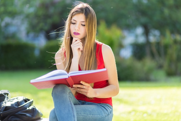 Giovane donna che si siede in un parco e leggendo un libro