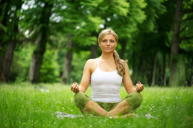 Giovane donna che si siede nella posizione di yoga nel parco