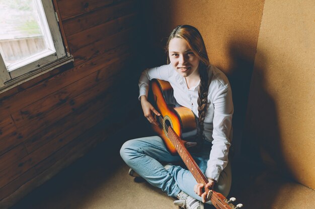 Giovane donna che si siede nella sala sul pavimento e suonare la chitarra a casa