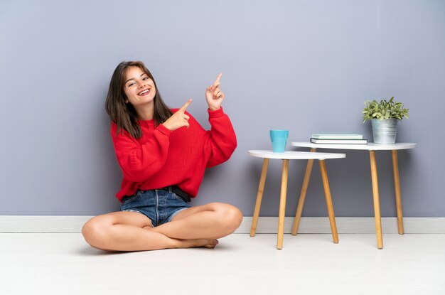 Giovane donna che si siede sul pavimento che indica con il dito indice una grande idea