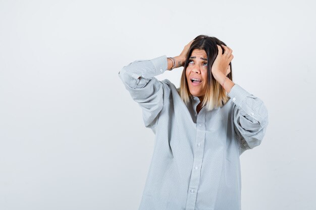 Giovane donna che si tiene per mano sulla testa in maglietta oversize e sembra infastidita. vista frontale.