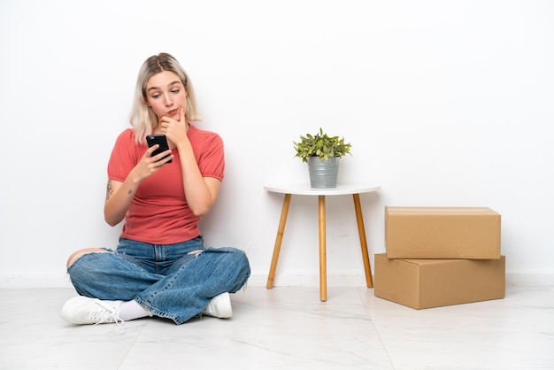 Giovane donna che si trasferisce in una nuova casa tra scatole isolate su sfondo bianco pensando e inviando un messaggio
