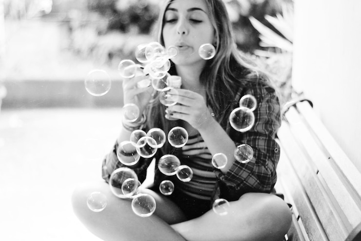 Foto giovane donna che soffia bolle di sapone mentre è seduta su una panchina