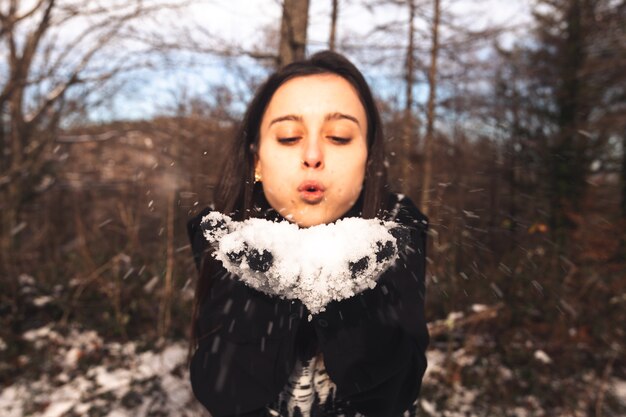 Giovane donna che soffia neve sulle sue mani