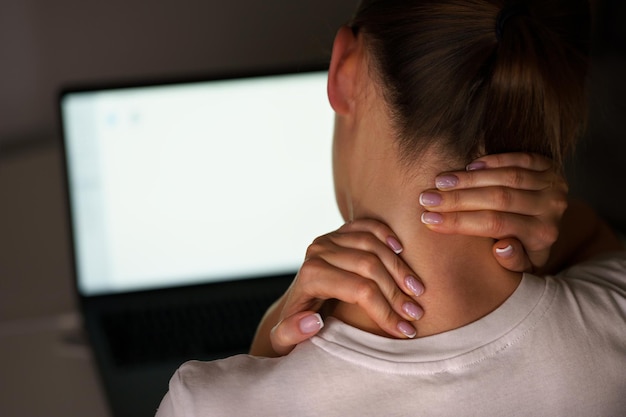 Giovane donna che soffre di dolore al collo dopo aver lavorato al computer Massaggiare il collo per alleviare il dolore