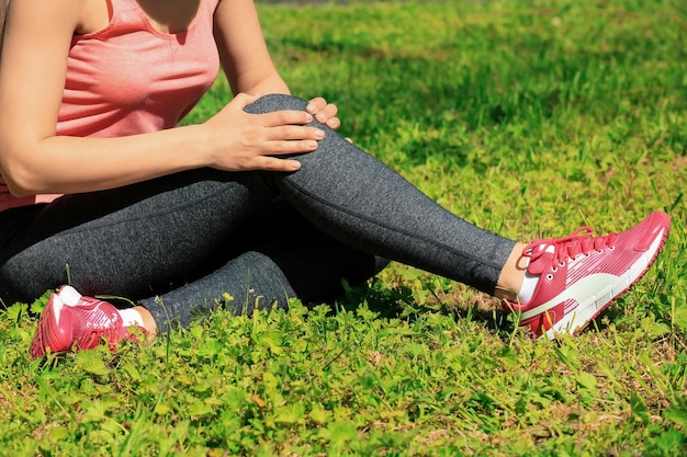 Giovane donna che soffre di dolore alla gamba mentre si siede sull'erba all'aperto